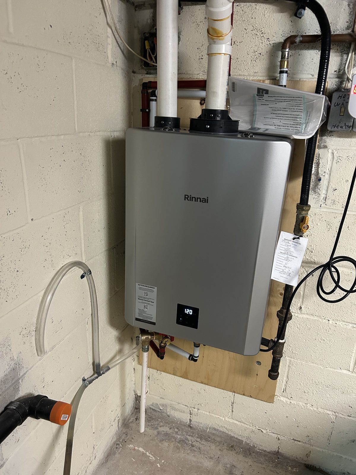 Rinnai tankless water heater mounted on a backboard with gas shut-off, PVC venting, and condensate drain