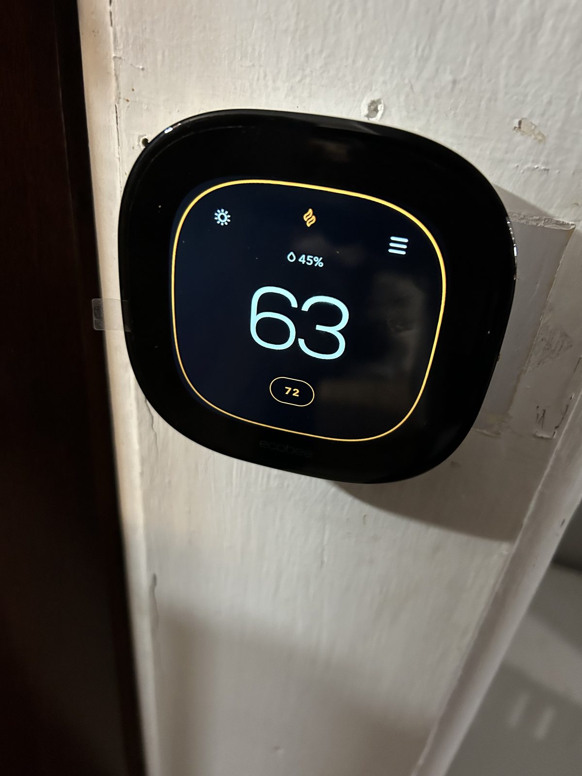 Ecobee smart thermostat mounted on a wall showing indoor temperature and humidity